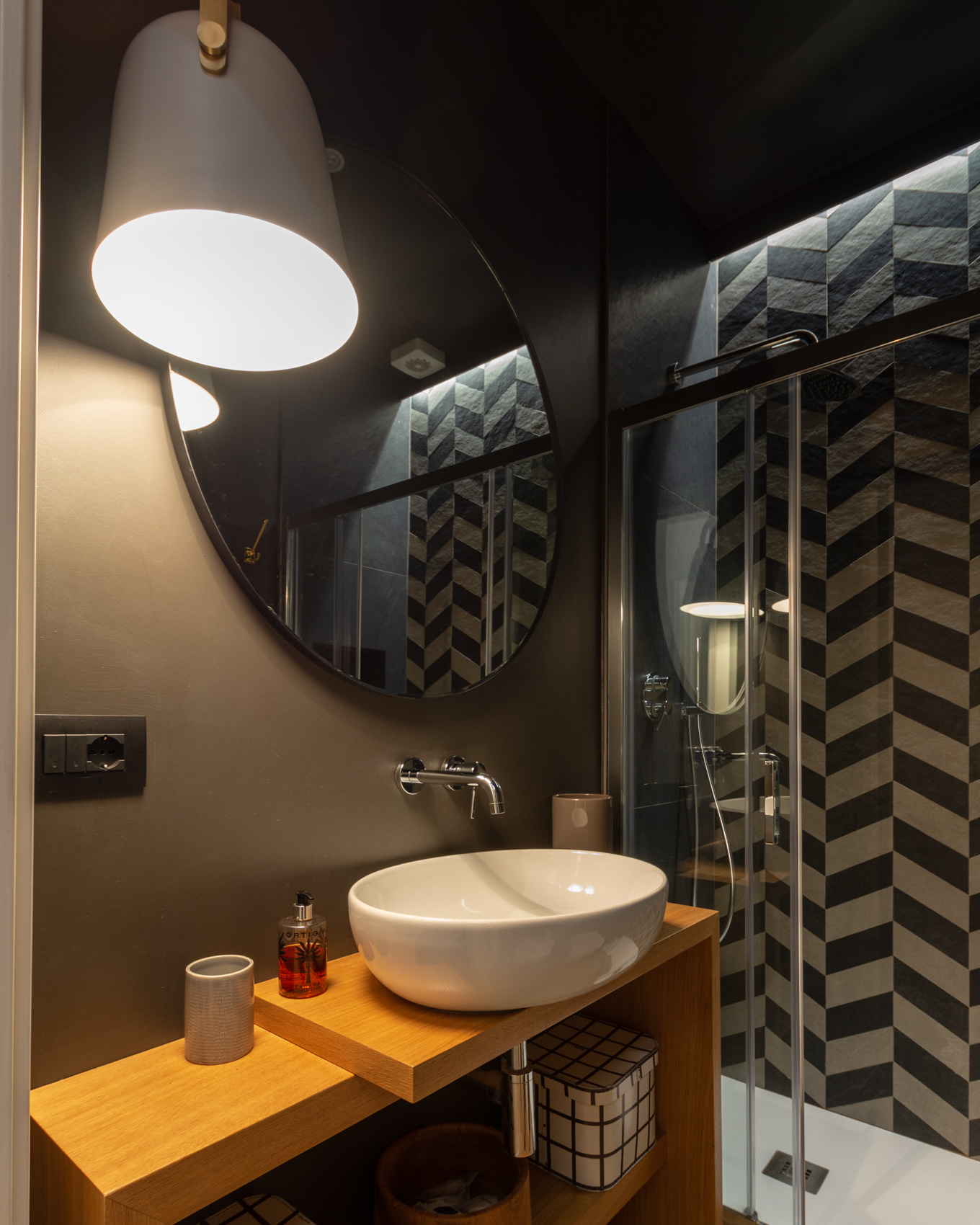 Bathroom with round mirror, white basin and herringbone-tiled shower