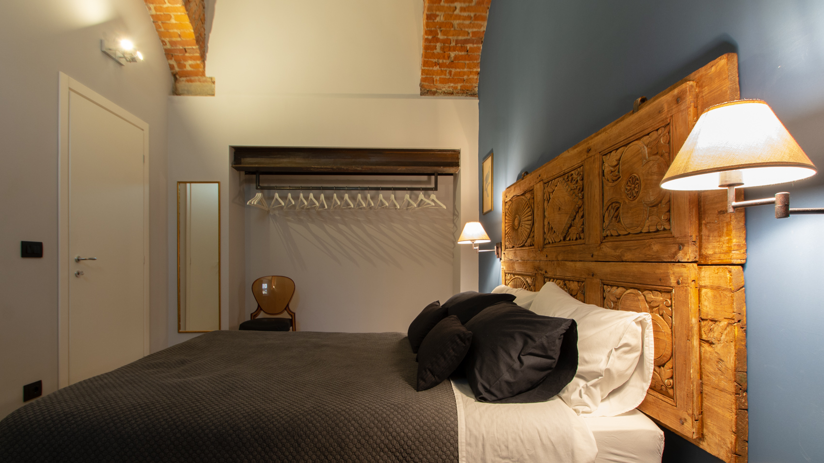 Bedroom one with open wardrobe and carved headboard under vaulted ceiling