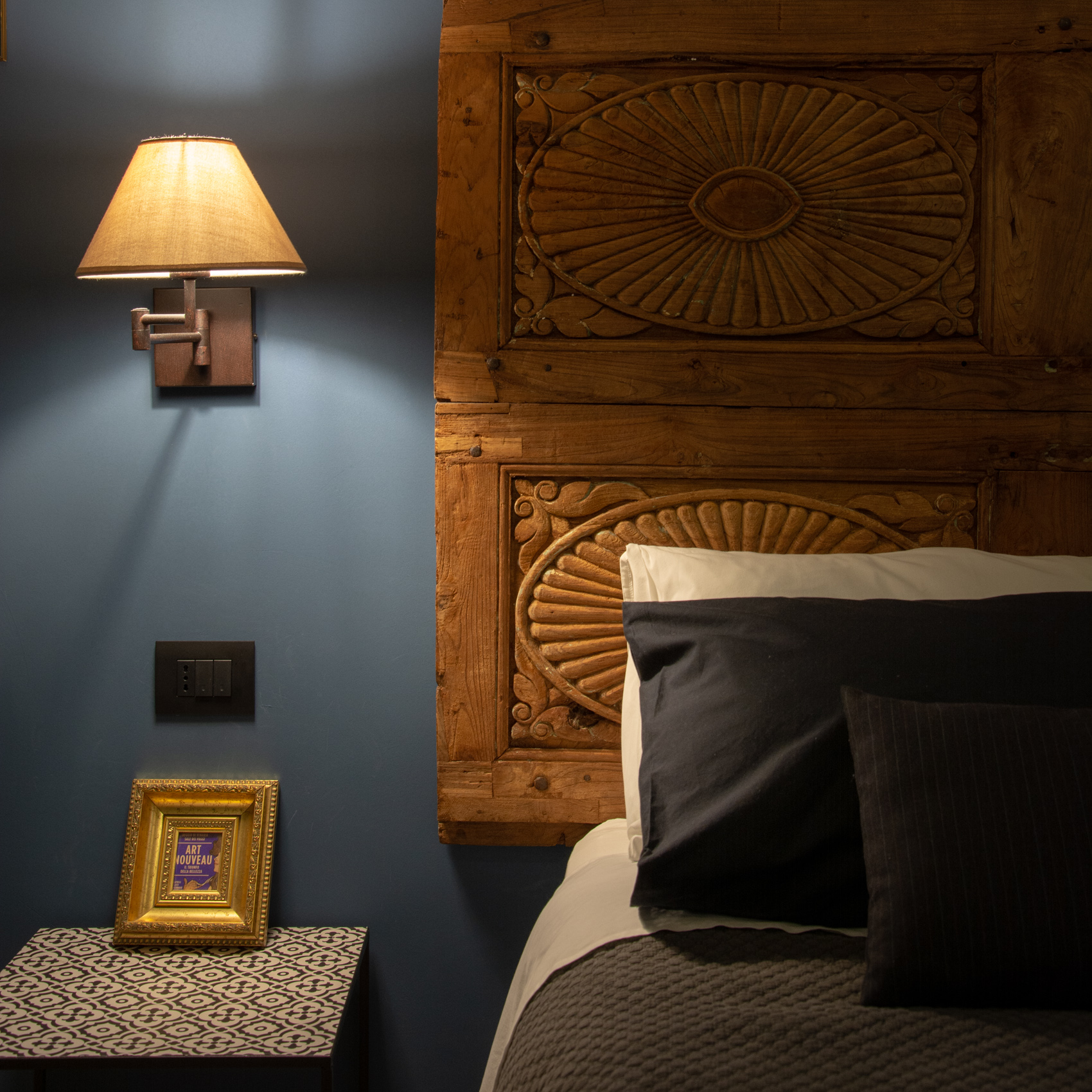 Carved headboard detail with wall lamp and framed artwork