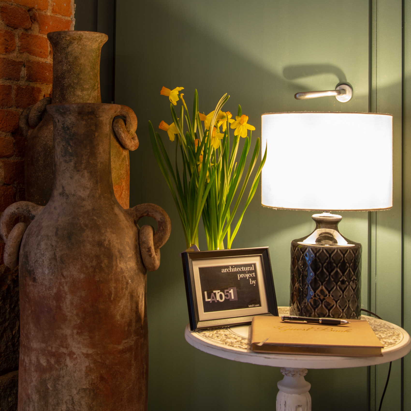 Decorative detail: terracotta amphora, daffodils and lamp against brick