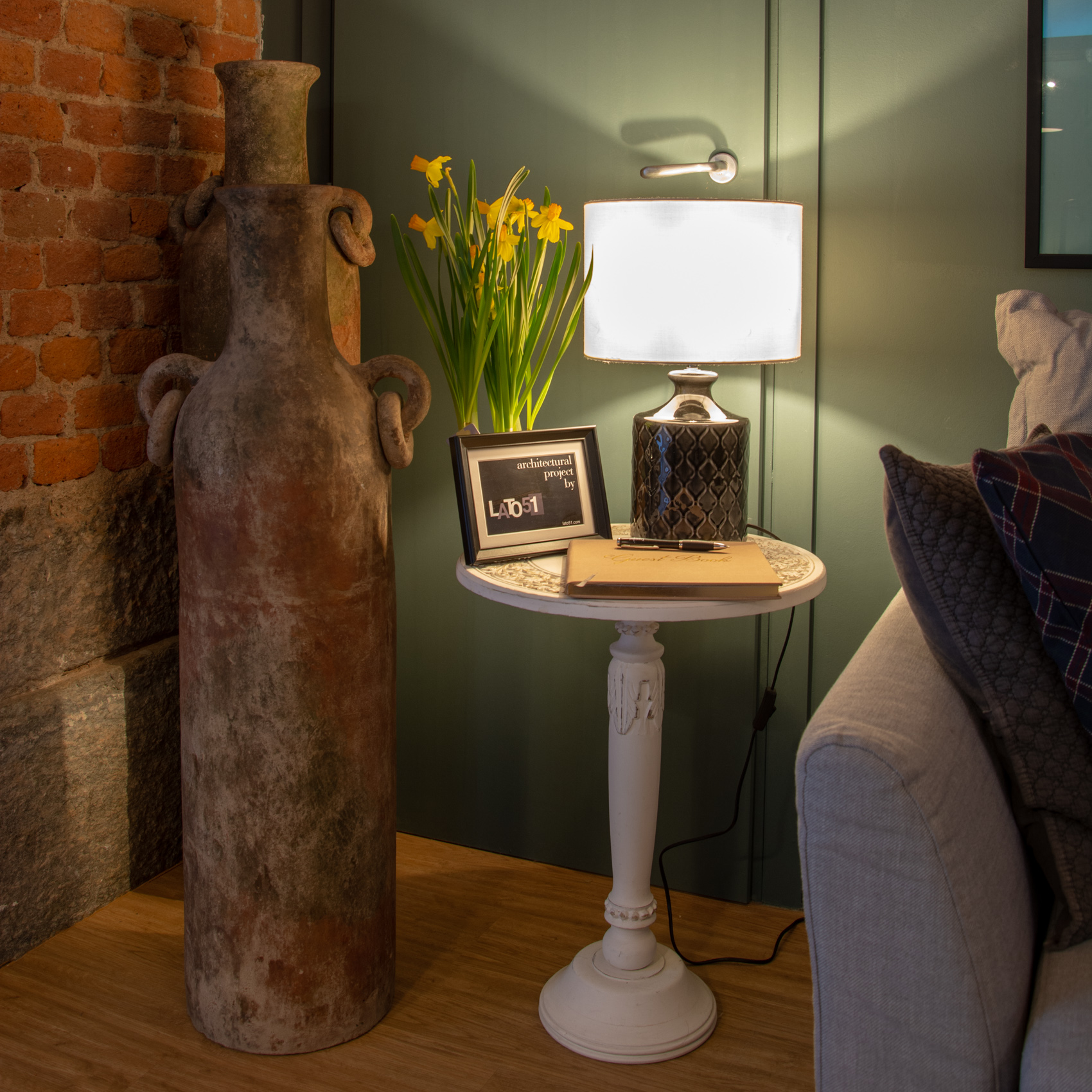 Living room corner with table lamp, terracotta amphora and deep green wall